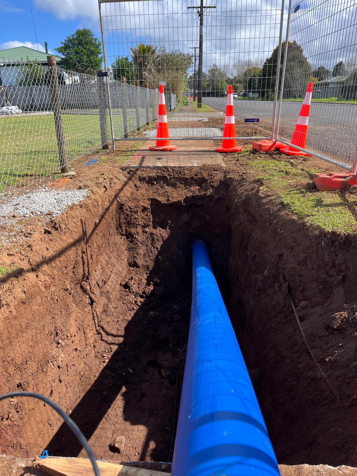 blue pipe installed in trench dug under a pavement alongside a street