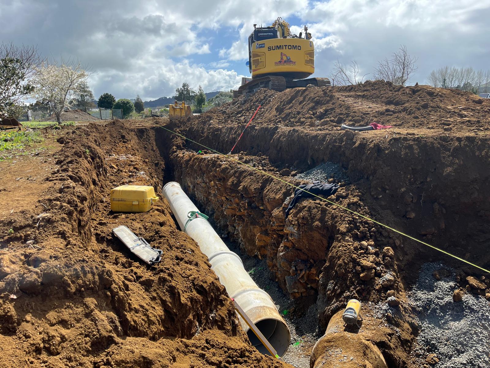 Pipe laid in deep trench, digger above next to trench