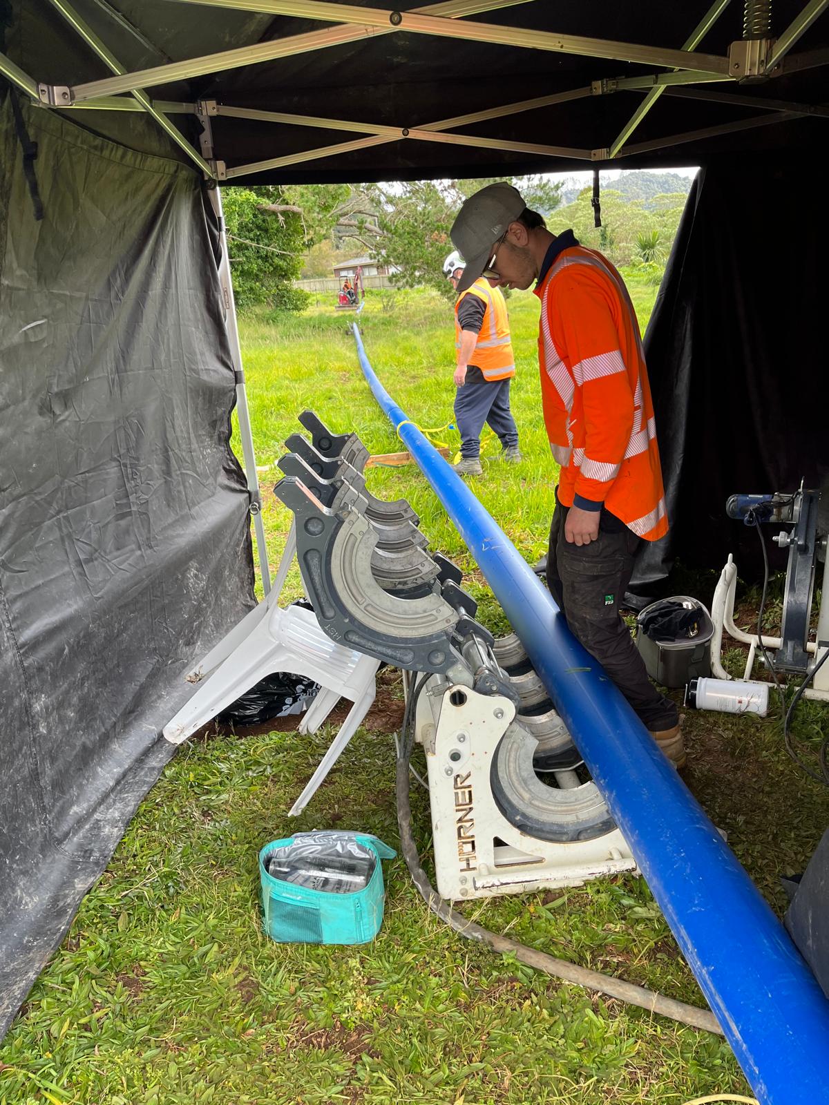 Worker preparing to weld blue pipe in enclosure